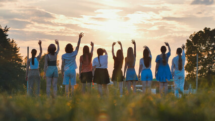 Students happily waving goodbye in a field against a beautiful sunset, celebrating the end of school and the beginning of summer