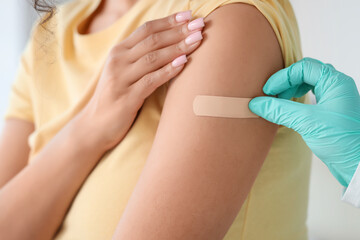 Female doctor applying medical patch on woman's arm after vaccination in clinic, closeup