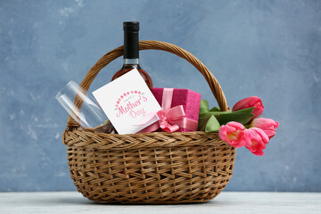 Basket with wine bottle, tulips and gift box for Mother's Day on table against blue grunge background