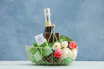 Basket with champagne bottle, tulips and chocolate for Mother's Day on table against blue grunge...