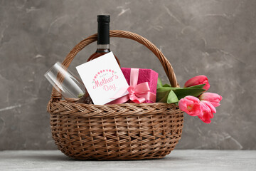 Basket with wine bottle, tulips and gift box for Mother's Day on table against grey grunge...