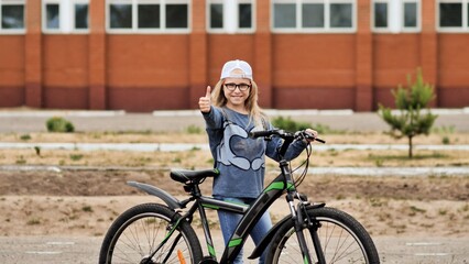 Obraz premium Blonde little girl posing with her bicycle in the summer in the city.