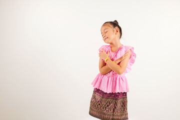 Portrait Thailand kid girl smiling traditional Thai dress costume hugging herself remember moment, studio isolated white background, kindergarten child love yourself carefree self care and self esteem