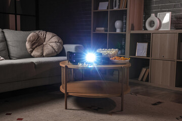 Modern video projector with tasty snacks on table in dark room