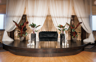 A stage with a black velvet sofa for the wedding ceremony indoors. Stage decoration with a small sofa and white curtains behind creates an atmosphere for presentations or creative meetings