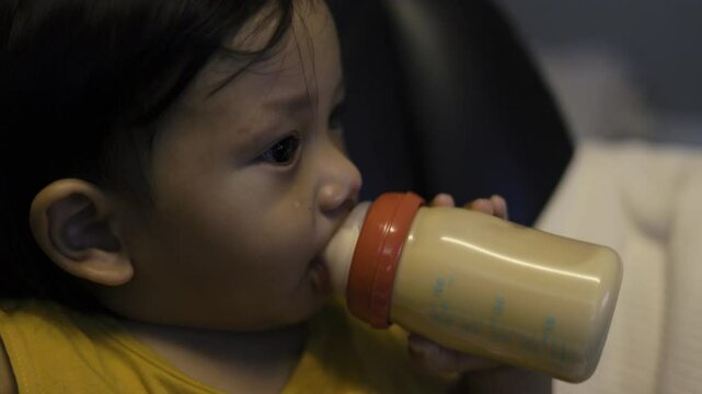Little cild sitting on the bed and holds in his hands a bottle of milk.