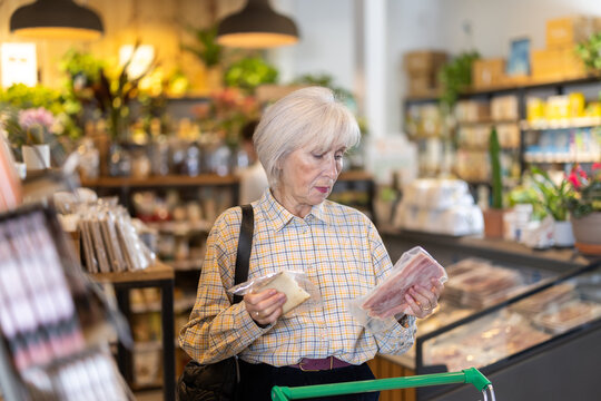 Elderly woman buyer chooses fresh cheese and bacon meat in eco grocery supermarket