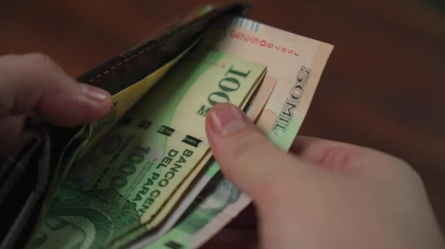 Man's hands checking one-hundred-thousand and fifty-thousand guaran&iacute; bills from Paraguay