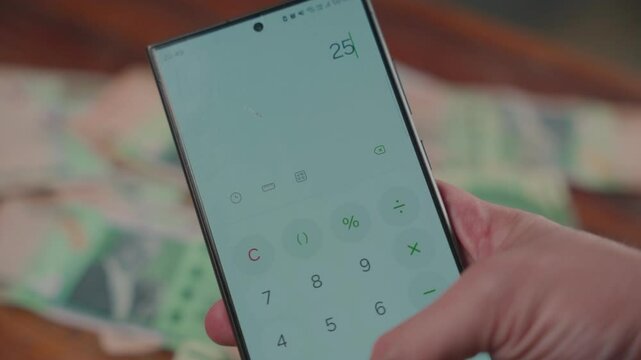 Man's hand using a cellphone calculator with Paraguayan guaran&iacute; bills in the background