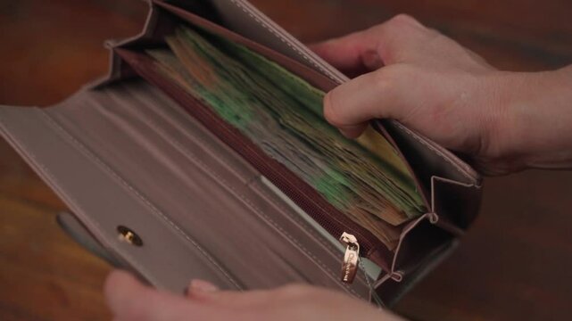 Woman's hands checking wallet with one-hundred-thousand guaran&iacute; bills from Paraguay