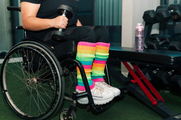 Obraz premium View of a woman in a wheelchair and her hands, exercising and carrying dumbbells, in a gym, view of a woman's hands with dumbbells in a wheelchair.