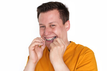Close-up of smiling young man adjusting his braces with fingers on a white background