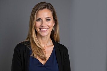 Obraz premium Portrait of a Smiling Caucasian Woman in Her 30s with Medium-Length Brown Hair, Wearing a Dark Cardigan against a Gray Background