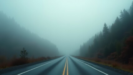 Wet mountain road disappearing into dense fog with misty hills and forest	