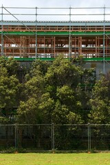 Obraz premium Construction Site with Scaffold Behind Lush Trees - Urban Meets Nature