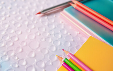 Fototapeta premium Close-up top view of colorful stationery items arranged on a textured light surface. Pencils, pen, and notebooks are neatly placed, creating a bright and organized scene.