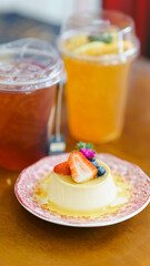A creamy dessert topped with fresh strawberries and blueberries, served on a decorative plate, with beverages in the background.