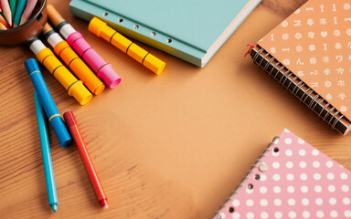 Colorful markers, pencils, and notebooks are arranged on a wooden desk surface, suggesting a creative workspace or study area ready for use.