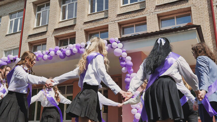 Students wearing purple ribbons joyfully dancing in a circle in front of their school to mark the...