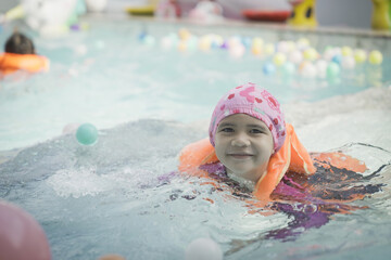 A young girl is in the water wearing a pink hat and a life jacket. She is smiling and looking at...