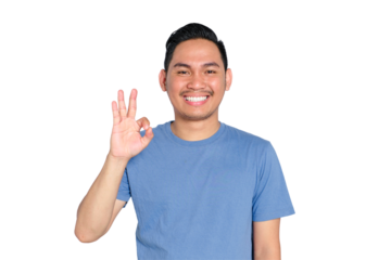 Smiling young Asian man showing OK hand gesture, wearing blue t-shirt, isolated on transparent background