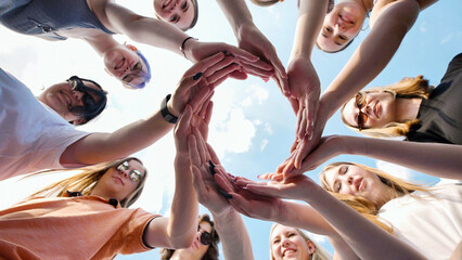School friends unite to form heart shape with hands against blue sky, symbolizing teamwork and friendship