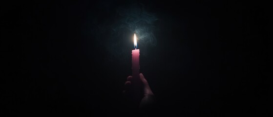A hand holds a burning candle in the dark, smoke rising.  A single light source against the black background