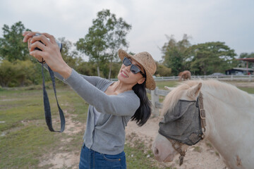 A female tourist visits a horse farm and takes selfies with horses.