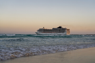 Obraz premium Cruise ship on the ocean. Luxury liner at sunset. Miami Beach with cruise ship. Turquoise water and cruise liner. Tourist cruise ship near the coast. Ocean waves and vessel boat.