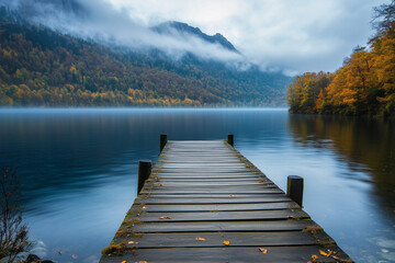 Fototapeta premium Wooden Pier on Serene Lake During Autumn with Misty Mountain Backdrop