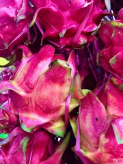 A vibrant pink and green pile of dragon fruits with a spiky, leathery texture, likely displayed for...