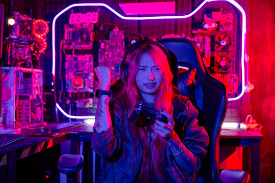 Gamer using joystick controller for virtual tournament plays online video game with computer neon lights dark room, woman wear gaming headphones playing live stream esports games console at home