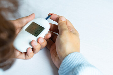 Woman's hands checking diabetes and hyperglycemia with digital blood sugar meter. Healthcare and...