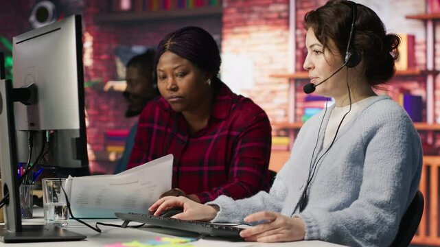 Call center team leader going over paperwork files next to colleague at PC desk. Customer support manager explaining company documentation to intern accommodating with job, camera A