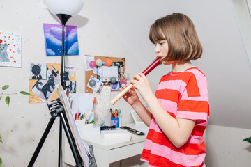 Young girl practicing flute at home in her room. Musical creativity and personal time. Music lessons at home. © Elena Medoks