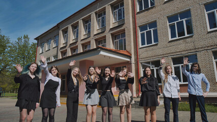 Obraz premium Joyful group of students waving in front of a school building on a sunny summer day, celebrating togetherness and success