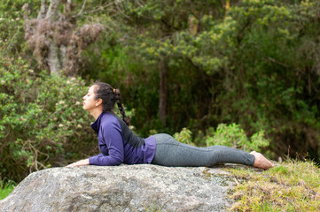 A woman is gracefully practicing a yoga pose on a natural rock formation outdoors