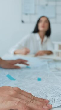 Skilled caucasian interior designer working with house model while discussing with asian architect engineer about house plan on meeting table with blueprint and house model scatter around. Immaculate.