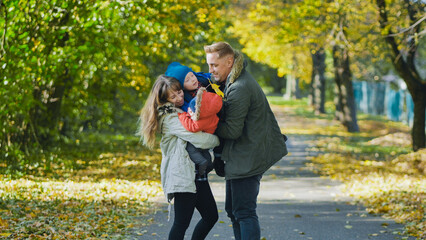 Obraz premium Parents playing with their two children in a park full of fallen leaves during a sunny autumn day