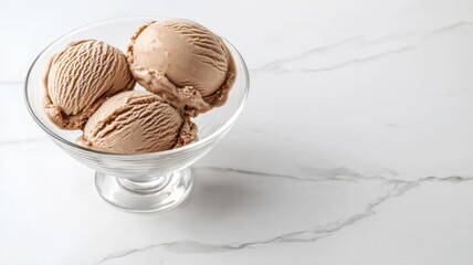 Three scoops of creamy chocolate ice cream in a glass bowl on a marble surface.
