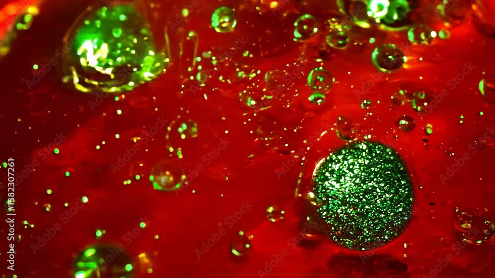 Poster dynamic drops of green glitter in red oil or ink diffusing through water, creating an abstract aquat