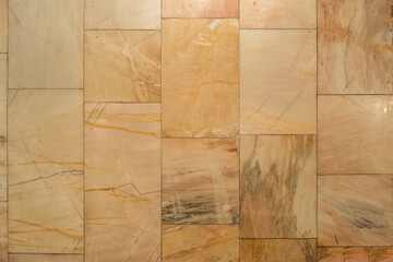 Wall covered with rectangular beige marble tiles. Natural stone surface with veins and texture,...