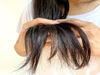A woman inspecting the ends of her hair, revealing visible split ends and frizz, possibly caused by...