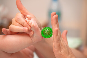A child's foot receives therapeutic massage with a green spiky Su-Jok ball for reflexology and...