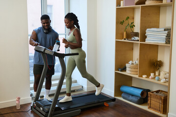 Couple exercising on treadmill with personal trainer guiding fitness routine