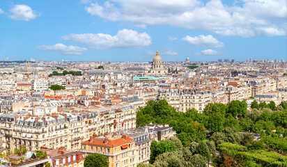 Aerial view of central Paris with Haussmann-era buildings, a lush park, and the golden dome of Les Invalides under a bright summer sky.