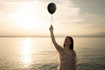 woman holding a black balloon by the string that wants to escape, concept of freedom