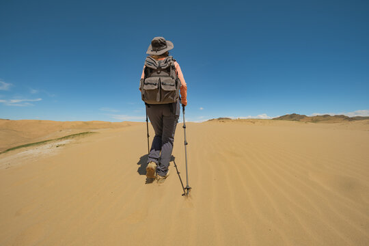 A traveler with a backpack on his back and trekking poles in his hands walks along the sand in the Gobbi desert in Mongolia. A man in the desert.