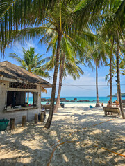 A serene beach on Koh Kham Island in Thailand features swaying palm trees and soft sandy shores. The tranquil turquoise water invites visitors to enjoy sunbathing and relaxation in paradise.