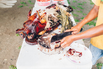 Man's hand slicing on wooden chopping board of the popular, delicious and crispy roasted pig known as "lechon baboy" (in the Philippines, Spain, Cuba, etc.). Selective focus. Copy space.